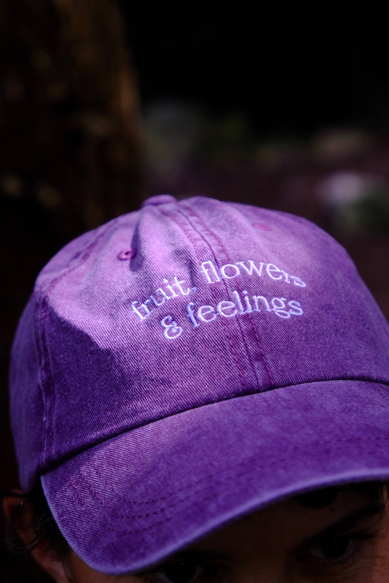 Purple cap with 'fruit, flowers & feelings' text on a blurred background
