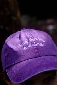 Purple cap with 'fruit, flowers & feelings' text on a blurred background