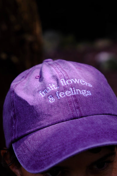 Purple cap with 'fruit, flowers & feelings' text on a blurred background